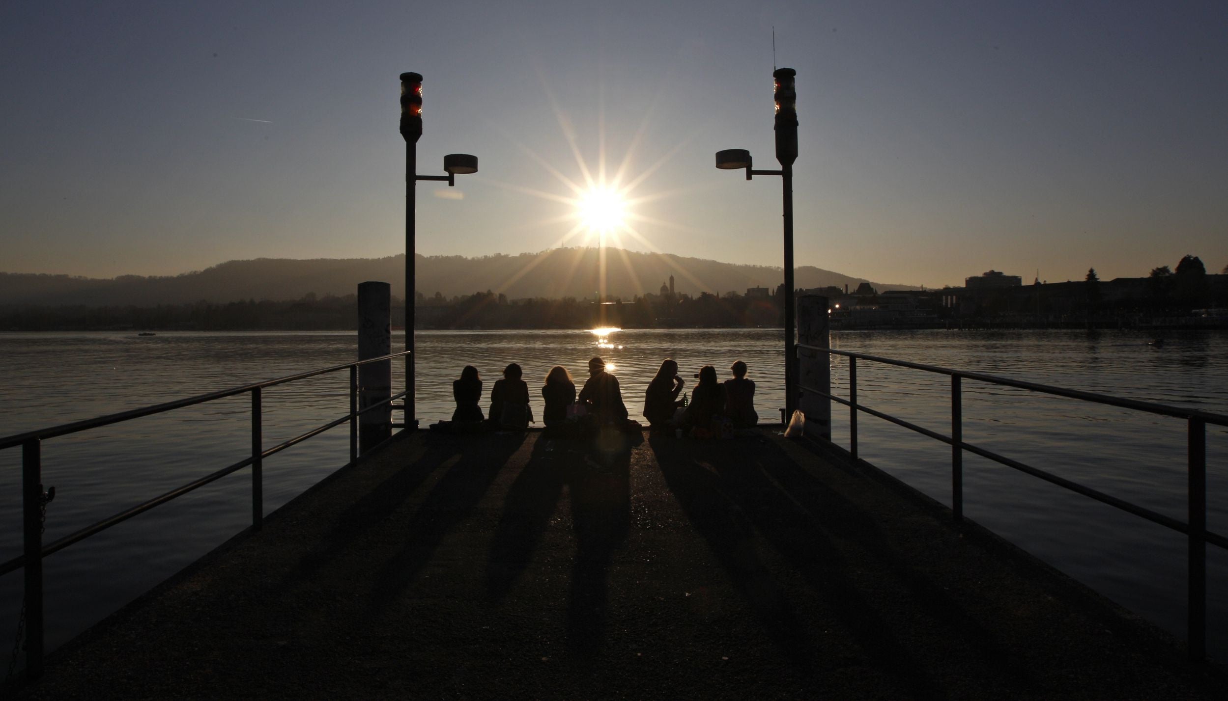 friends sitting on wooden dock during sunset