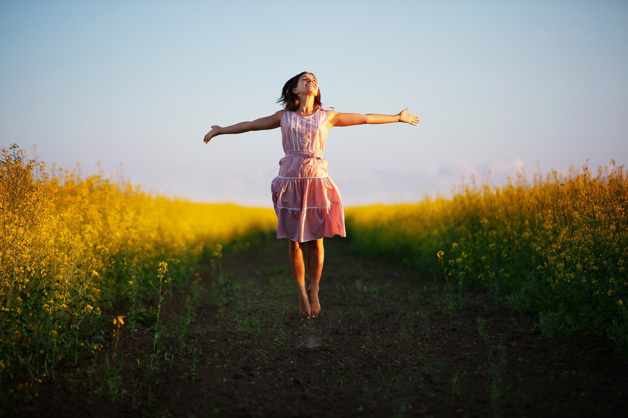 Young woman jumping in the middle of a field with yellow flowers