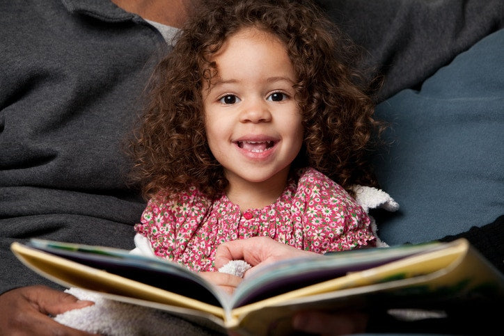 Happy curly little child girl is reading book
