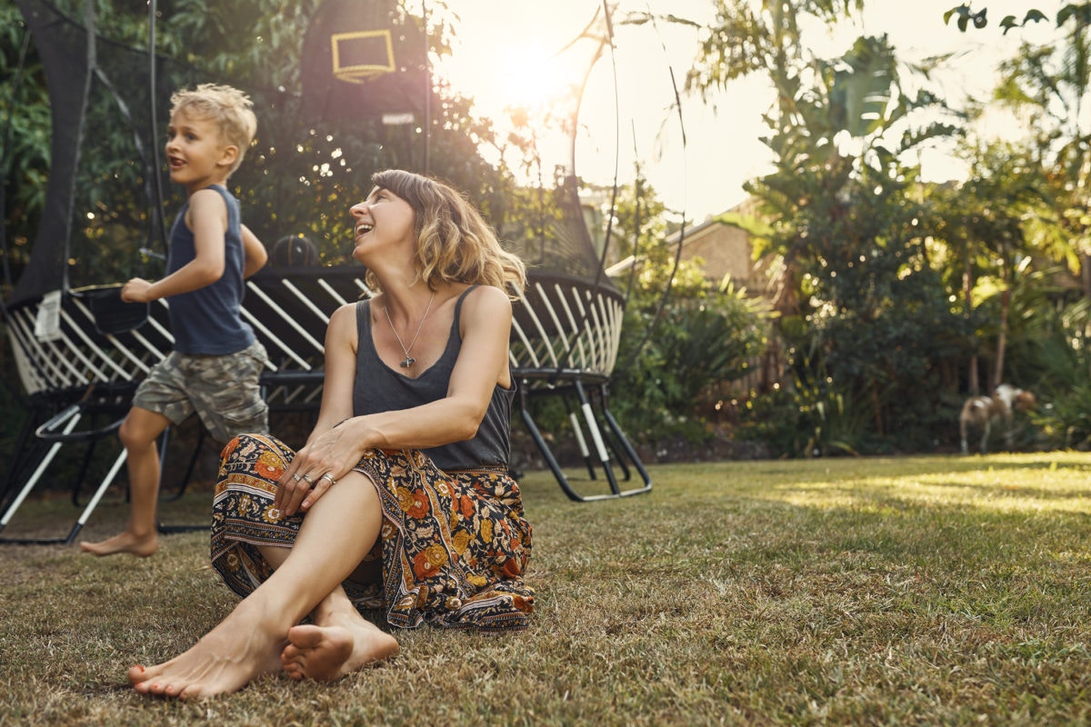 happy mother sitting while son running around in garden