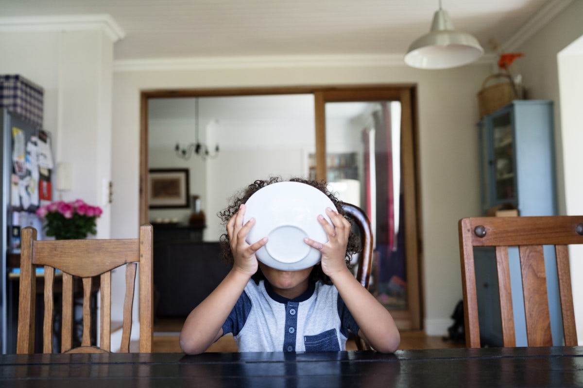 kid at a table holding a bowl of cereal