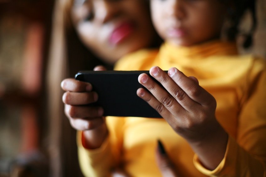 girl sitting on mom's lap and using smart phone