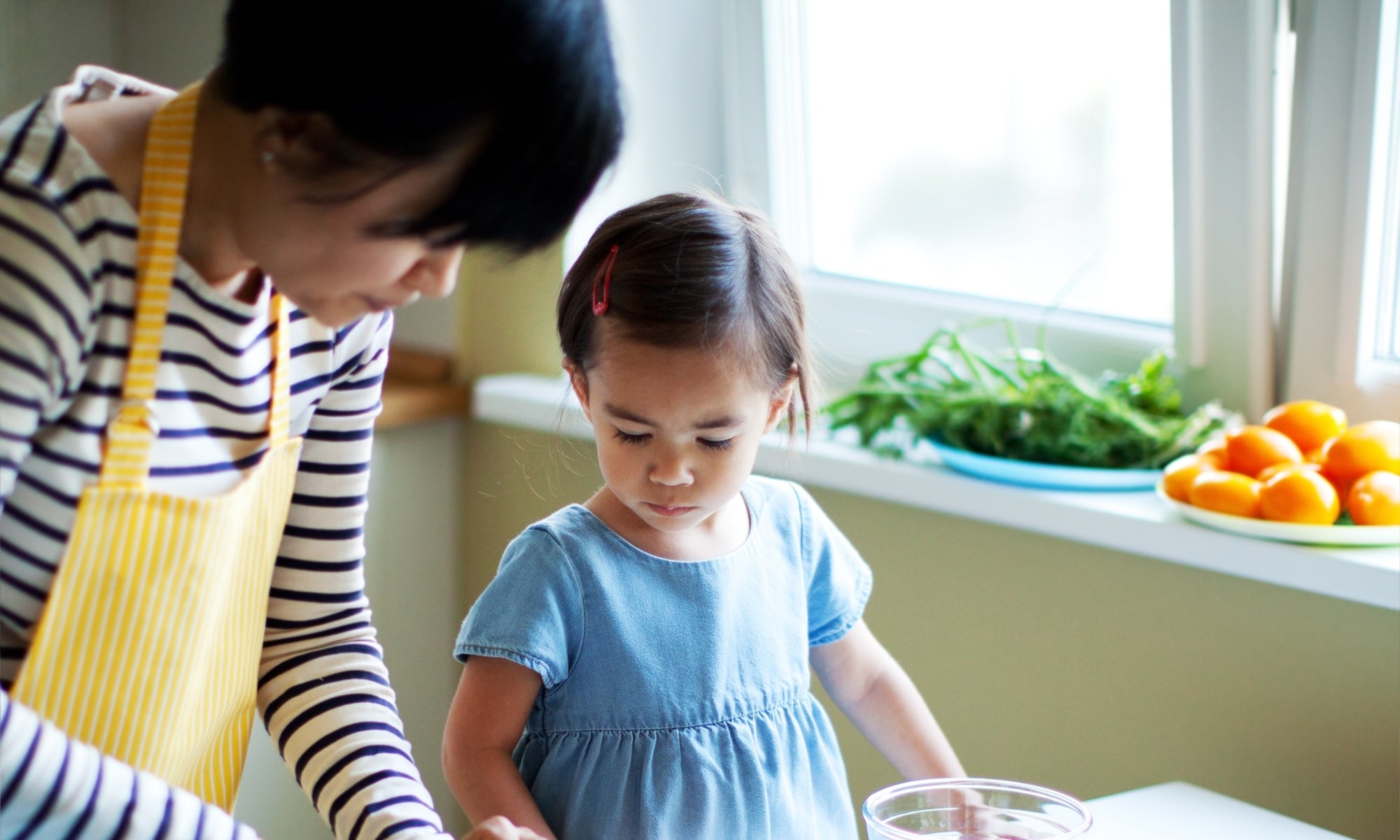 young girl looking at their mother who is cutting vegetables in the kitchen