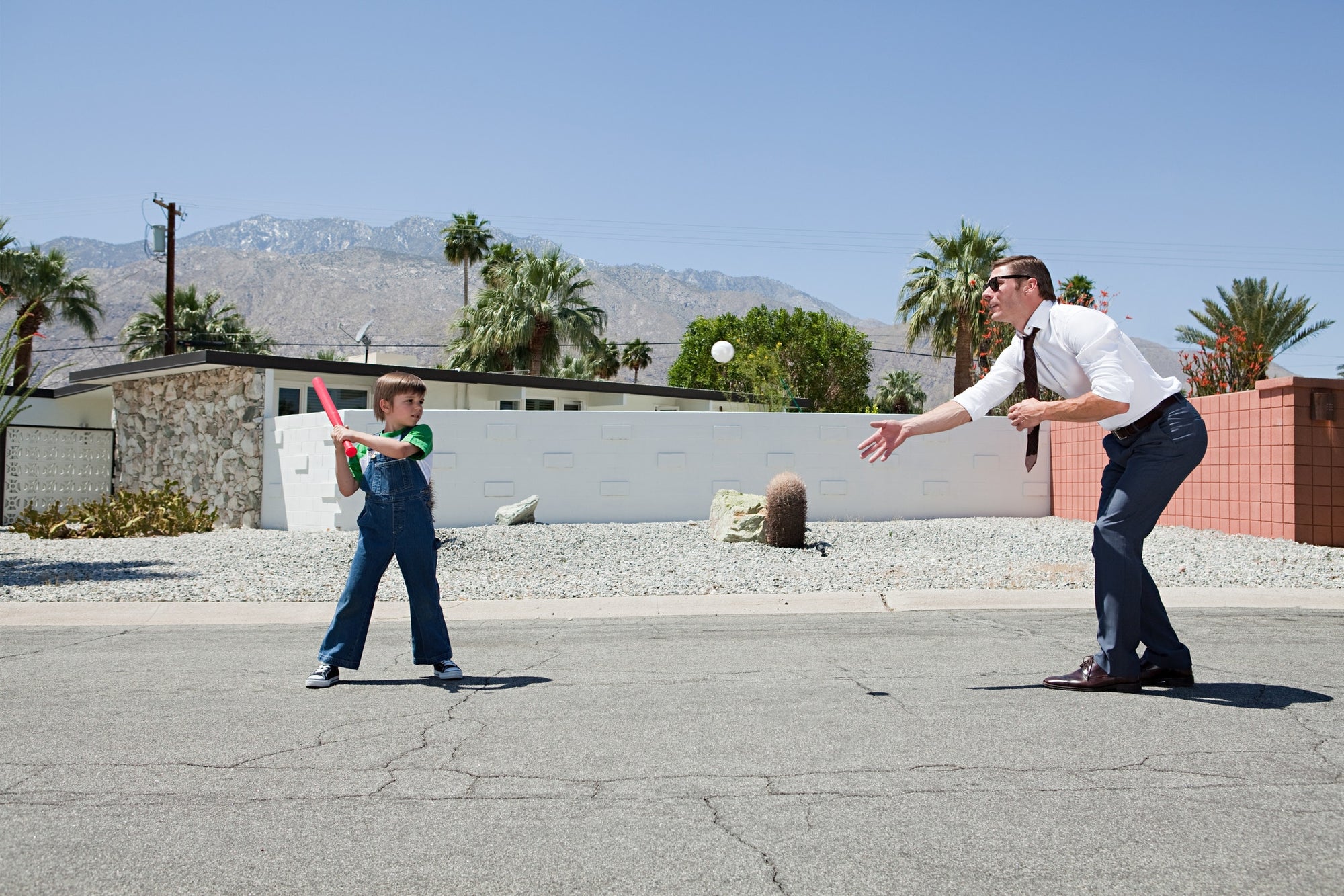 a boy playing with a man in a road infront of a house with white and red walls