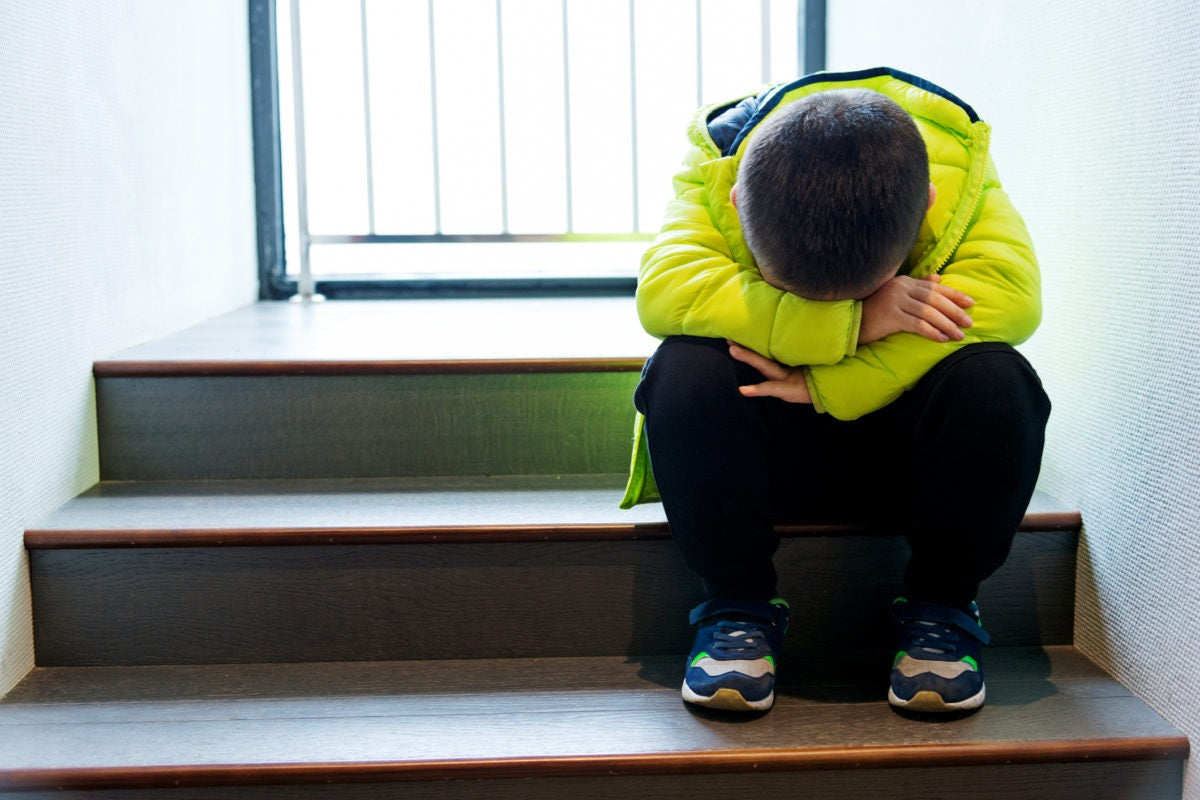 young boy sitting on the stairs in a closed position with his head down is feeling stressed