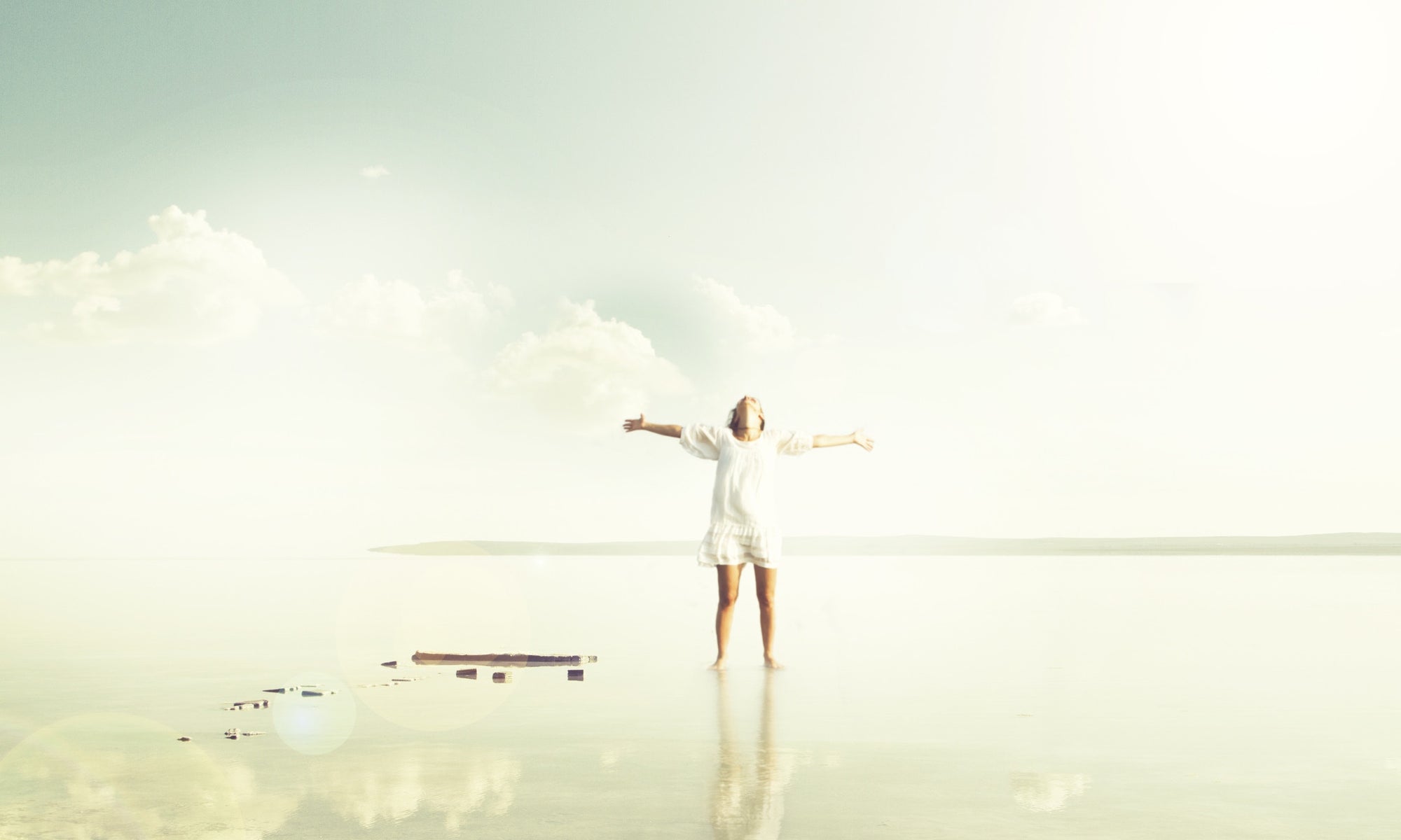 Young woman standing on the shore of scenic lake with her hands raised. 