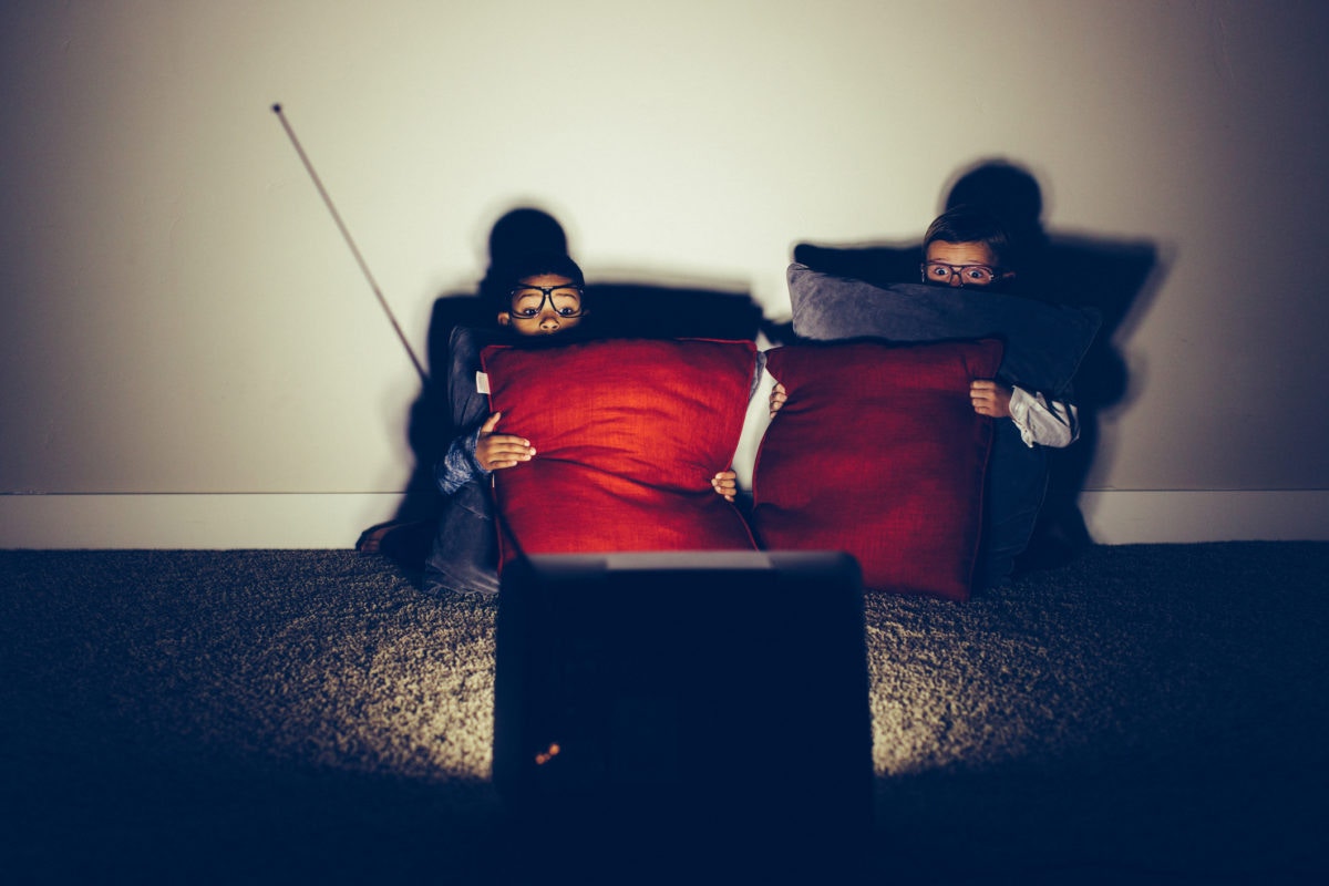 two boys holding pillows and watching scary movie