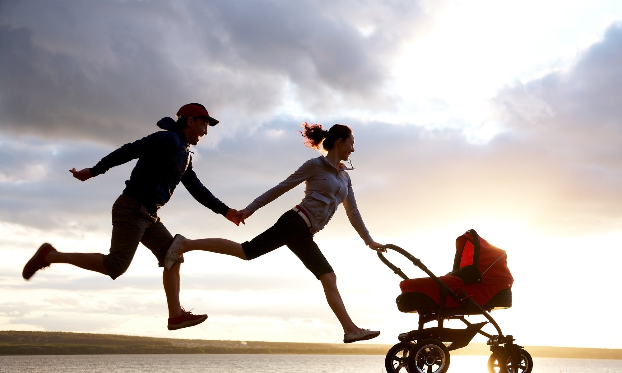 parents jumping in air with child in stroller