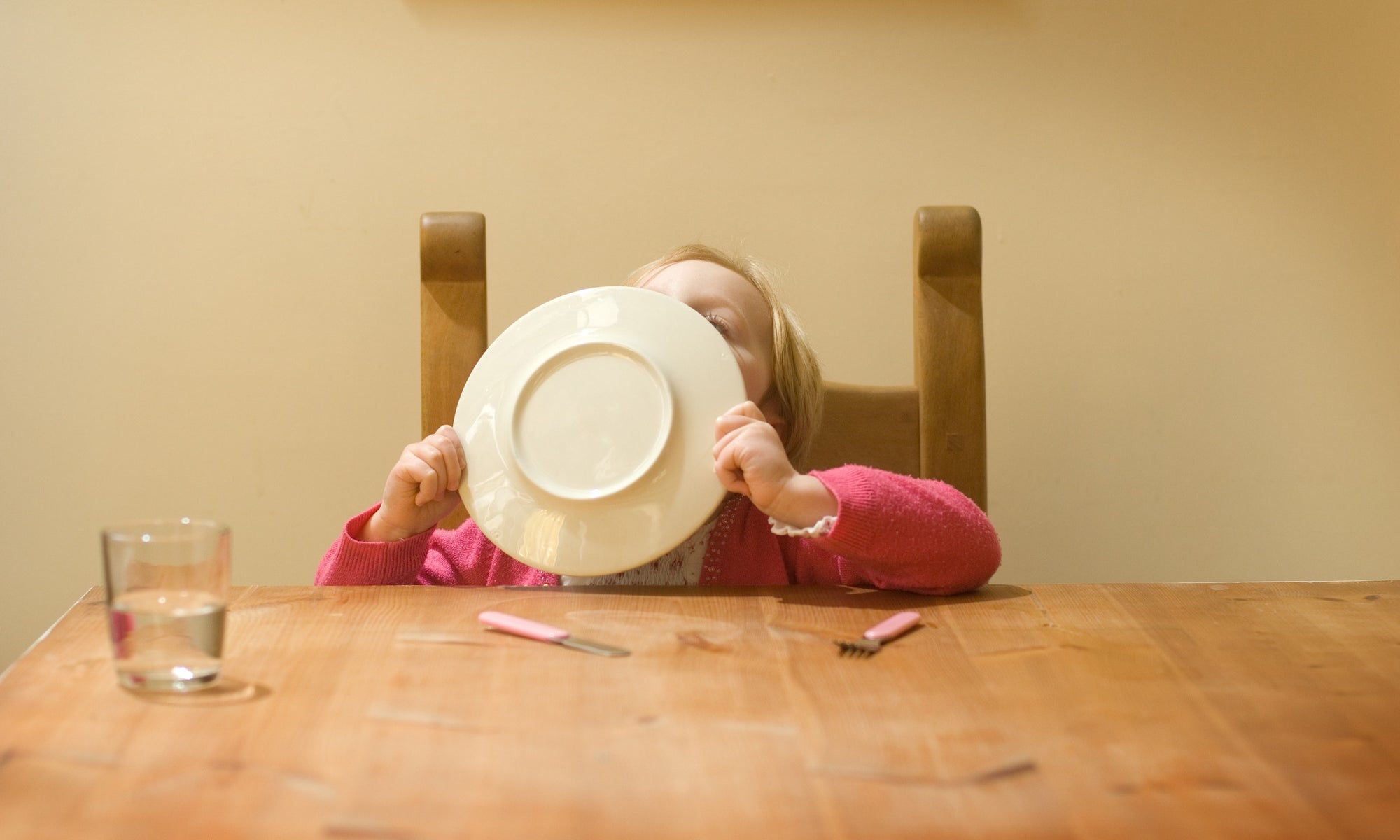 Child finishing food, cleaning plate using tongue, hiding face