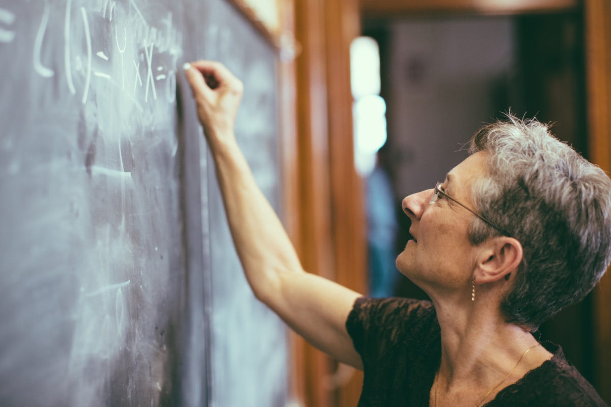 Teacher is teaching in a class room by writing something on a black board