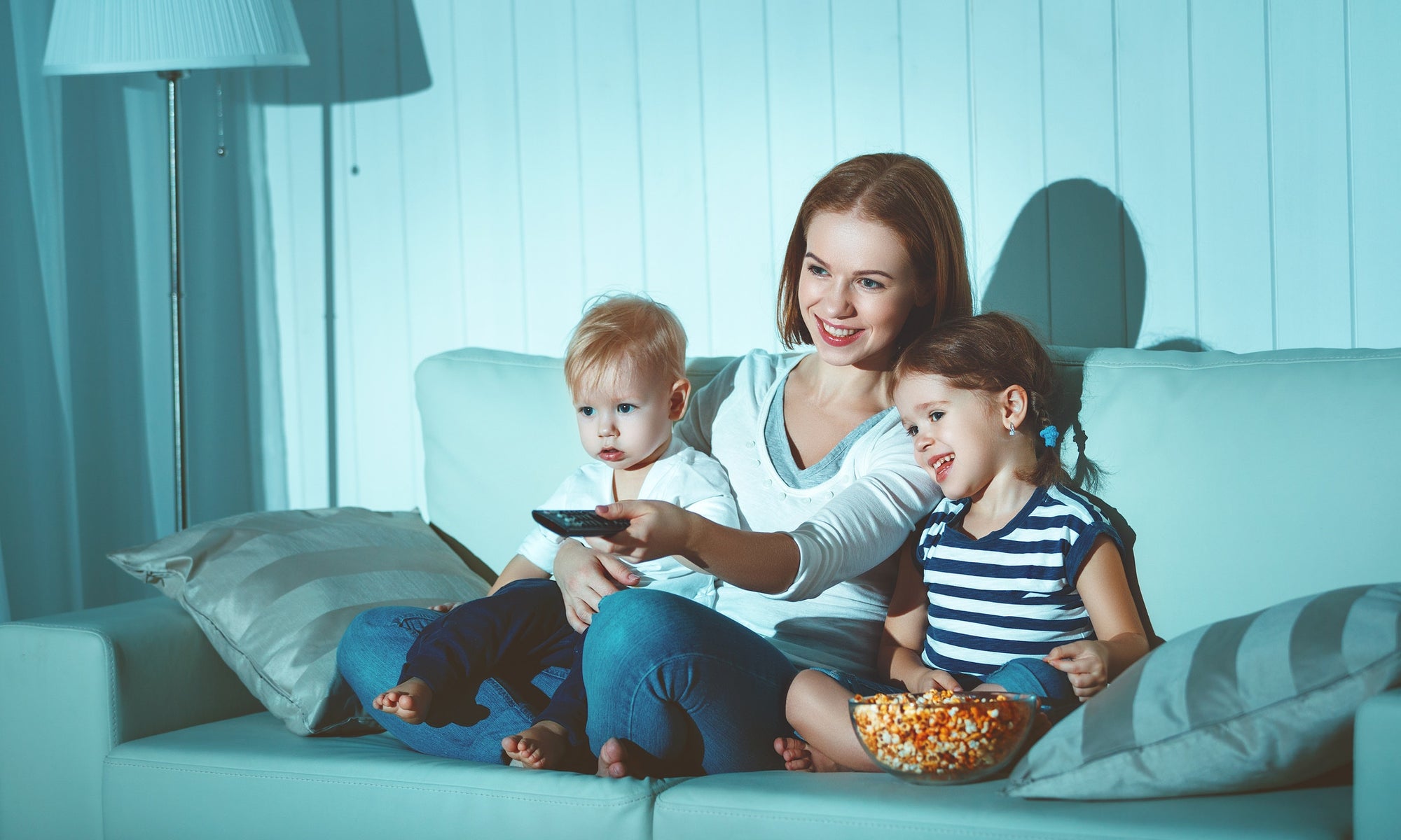 mother and two children sitting on sofa at home watching TV together