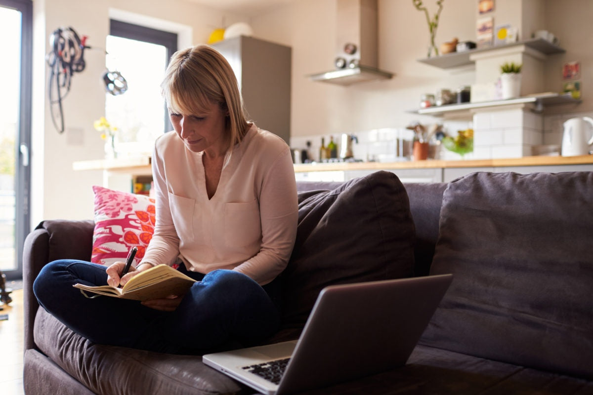 women sitting on couch with laptop and writing in notebook 