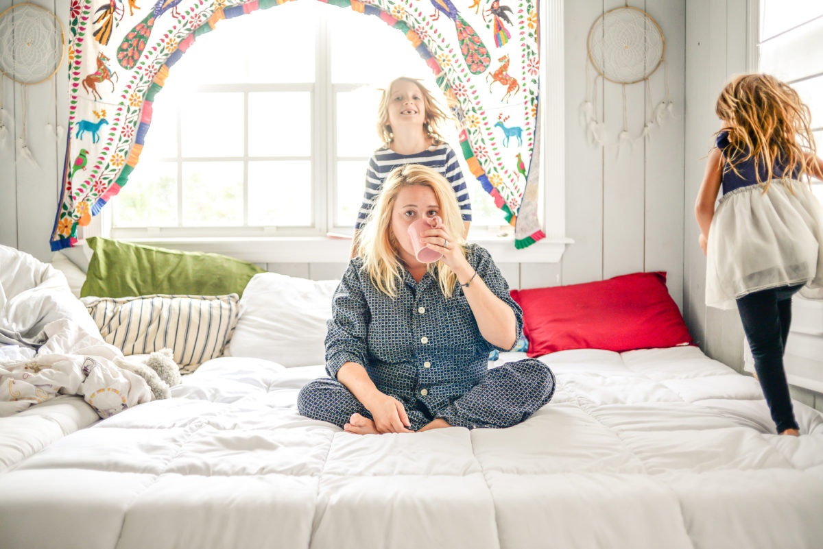 Mother having coffee, sitting on the bed with her children playing around her on the bed