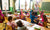 Kindergarten teacher and children with hands raised in classroom