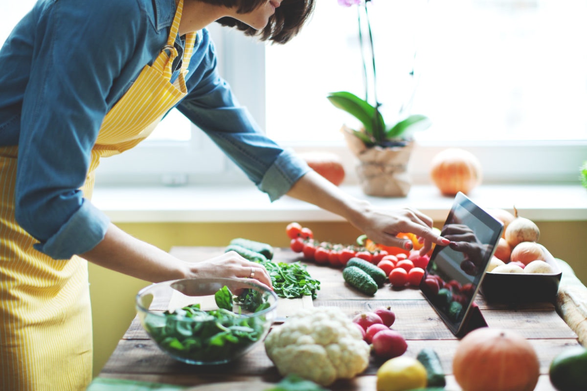 Woman cooking, swiping with a finger on a tablet screen watching for recipe