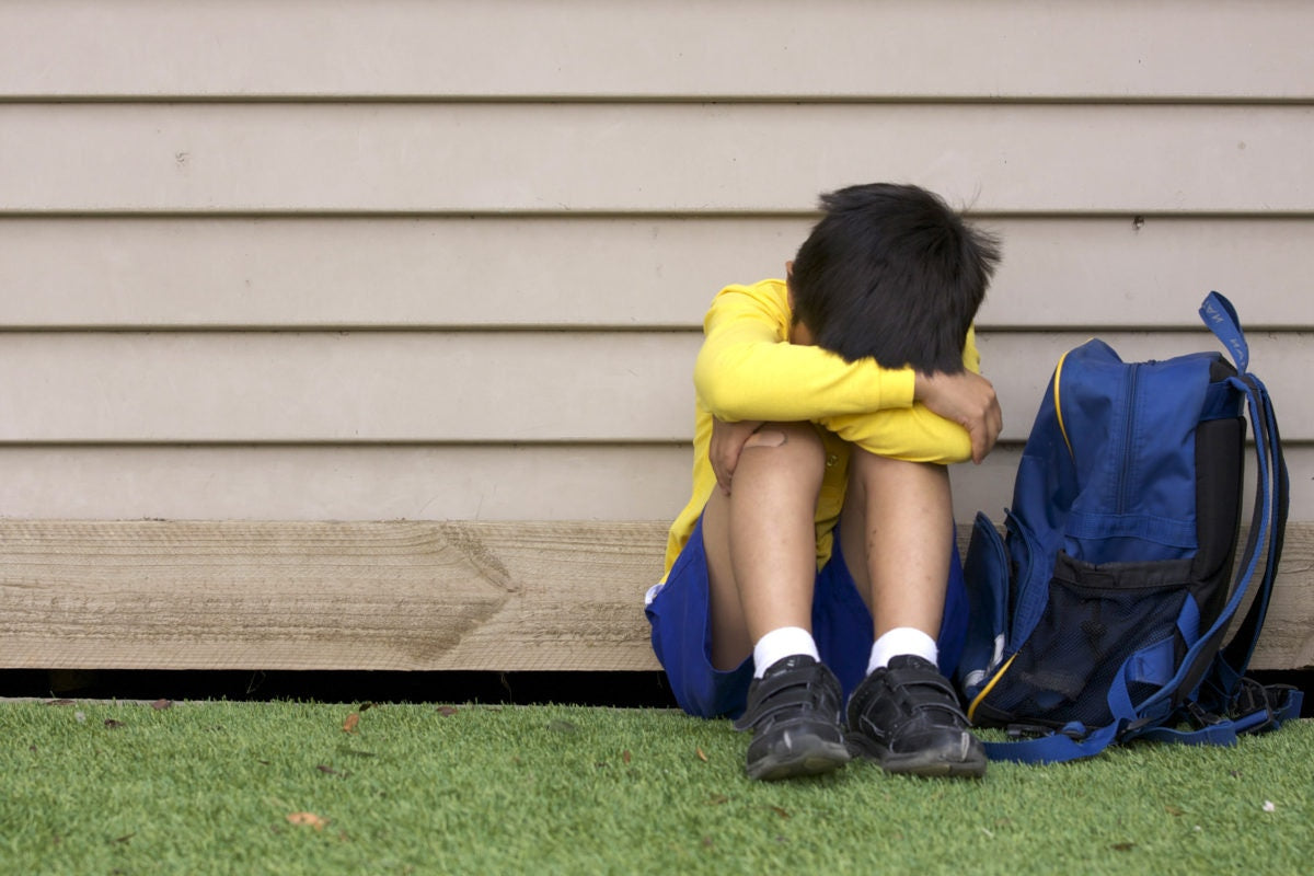 Boy sitting against a wall, backpack by side, looking down