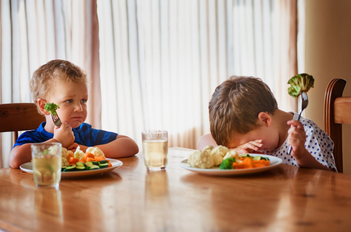 two kids not happy eating their vegetables