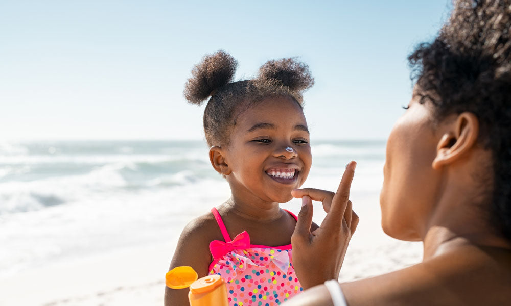 mother applying sunscreen on cute little black girl 