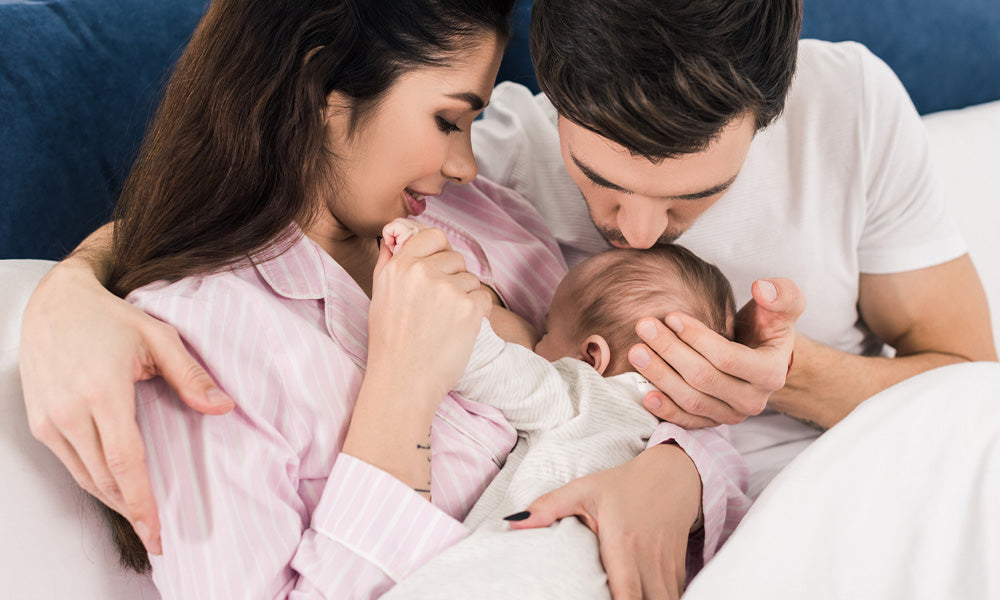 mother breastfeeding little baby with husband near by on bed