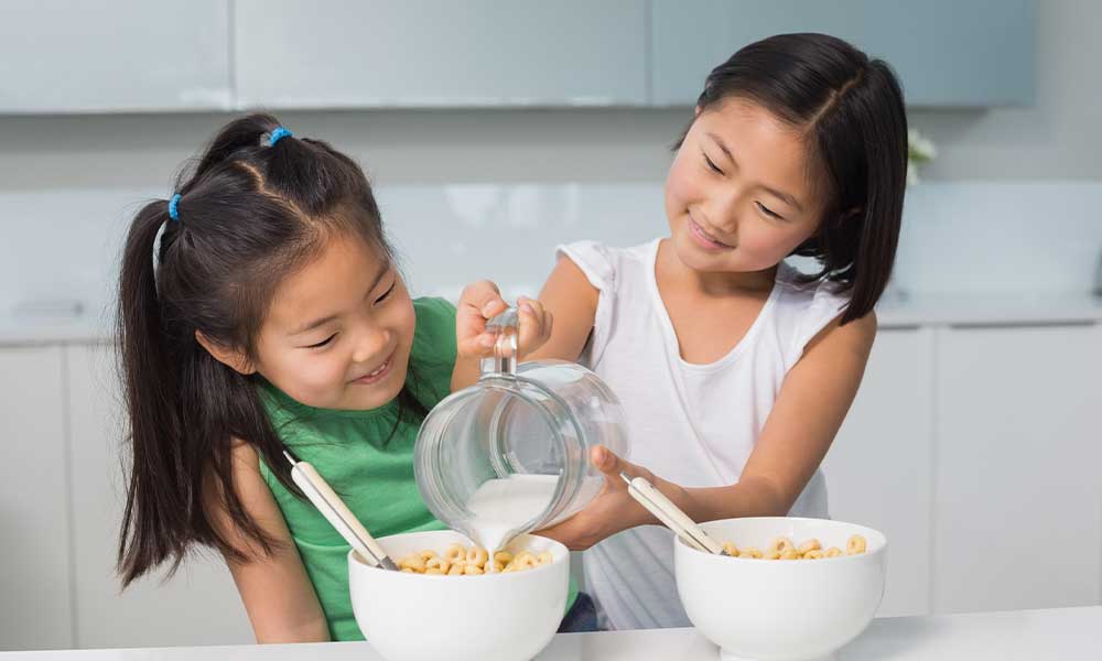 two happy young girls pouring milk