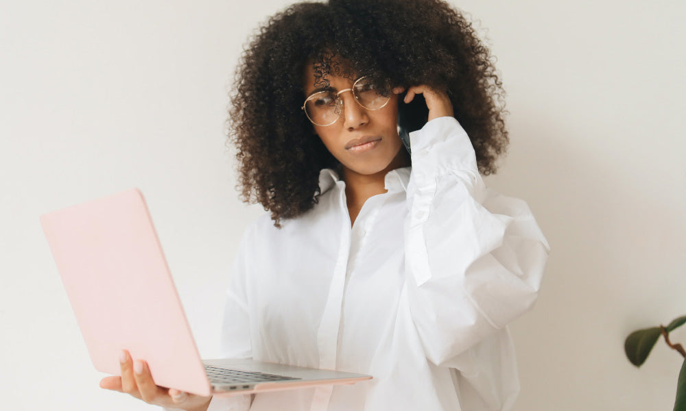 mujer mirando el ordenador sosteniendo el teléfono